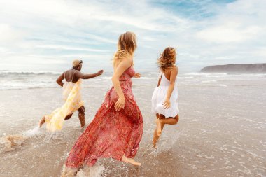 Üç genç kadın sahilde birlikte koşuyor. Arkadaşlarımla seyahat ediyorum..