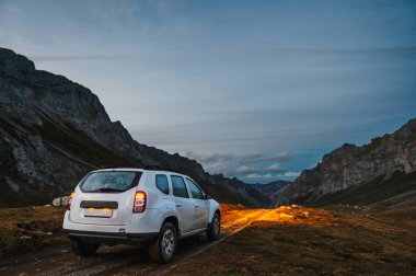 4WD 'li arazi aracı alacakaranlıkta ya da macera etkinliği sırasında bir dağın içinden ışık saçarak toprak yolda gidiyor..