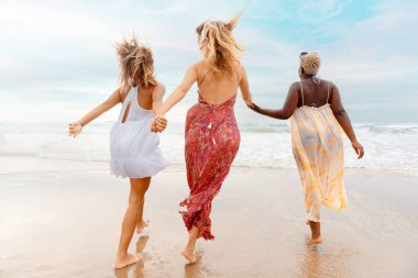 Üç kadın arkadaşın el ele tutuşup yaz gezisi sırasında sahile doğru yürüdüğü çok ırklı bir grup. Kadınlar arasındaki dostluk ve birlik.