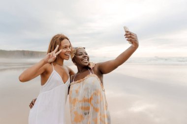İki arkadaş, yaz günü sahilde akıllı telefonlarıyla selfie çekiyorlar..