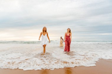 Yazlık elbiseler giymiş, deniz kıyısında sırılsıklam olmuş çok ırklı bir grup genç kadın. Yazın arkadaşlarıyla seyahat ediyor.