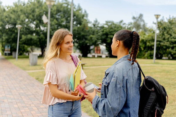 two young students with backpacks and school supplies chatting outside the university campus after class or during a break. inclusion and diversity at university