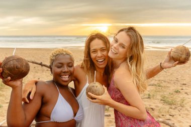 Mutlu bir arkadaş grubu yaz partisinde gün batımında sahilde içki içerken birbirlerine sarılıyorlar..