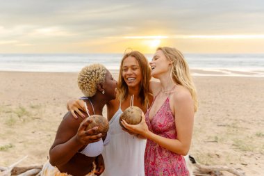 Gün batımındaki bir plaj partisinde hindistancevizinin içinde içki içerken eğlenen üç kadın arkadaştan oluşan çok ırklı bir grup..