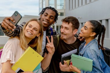 Çok ırklı bir grup öğrenci dersin sonunda akıllı bir telefonla selfie çekiyor.