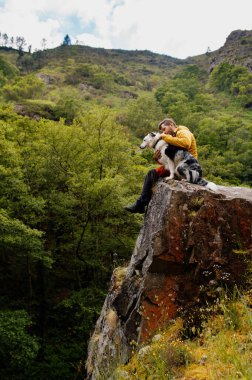 Bir uçurumun kenarında oturan bir adam, dağ yürüyüşü sırasında, sınırdaki çoban köpeğiyle birlikte orman manzarasını inceliyor. Hoces del Esva rotası, Asturias, İspanya.