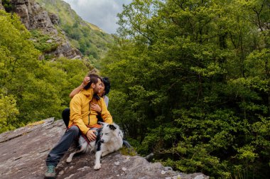 Bir çift yürüyüşçü, doğa yürüyüşü sırasında rahatlamak ve köpeklerine sevgi göstermek için otururlar. spor ve açık hava aktivitesi