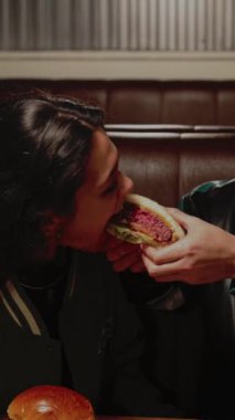 Genç bir adam romantik bir randevu sırasında kız arkadaşına bir restoranda hamburgerinin tadına bakar.