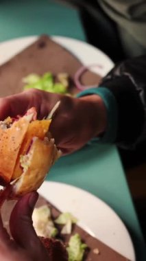 Hamburgeri ısıran genç adamın yavaş çekim dikey videosu.