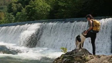 Yürüyüşçü, bir şelalenin yanında kayaların üzerinde dururken çoban köpeğini besliyor. Asturias, İspanya 'nın Cangas de Onis belediyesine bağlı bir somon çiftliği. Turist eğlencesi