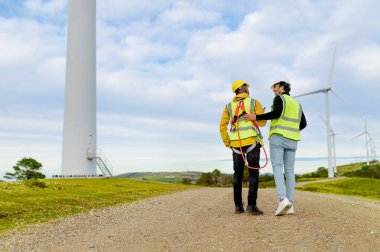 Bir rüzgar türbini parkında yürüyen ve konuşan mühendis ve operatör yenilenebilir enerji hakkında konuşuyor.