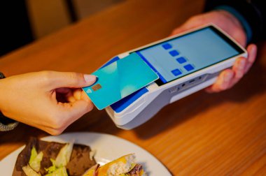 Fast food restoranında hamburgeri için bağlantısız kredi kartıyla ödeme yapan kadın.