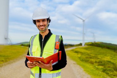 Rüzgâr santralinde gülümseyen ve tablet ve klasörü tutan genç mühendis