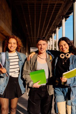 Kampüste ellerinde not defterleriyle dolaşan mutlu çok ırklı öğrenciler.