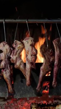 Yumuşak kuzu bacakları ahşap tükürük üzerinde yavaşça dönüyor, altın alevlerle yanan ateşin üzerinde ızgara yapıyor etin zengin yüzeyini karamelize ediyor.