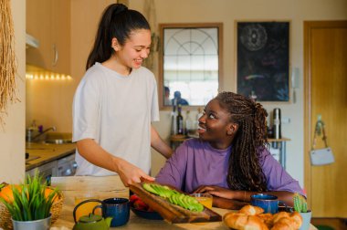 Lezbiyen çift, modern mutfaklarında avokado tostu, kruvasan, çilek ve portakal suyuyla sağlıklı bir kahvaltı yapıyorlar.