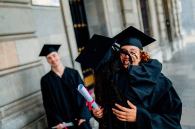 Mezuniyet töreninden sonra birbirlerine sarılan iki mutlu mezun başarılarını neşe ve heyecanla kutluyorlar.