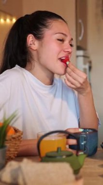 Genç Latin bir kadın kahve, çilek ve portakal suyu içiyor, ekranın dışında başka biriyle sohbet ediyor ve gülüyor.