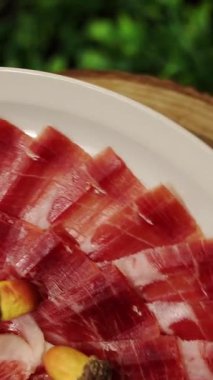 İberya meşe palamudu jambonuyla beslenmiş, dilimlenmiş ve bir tabağa yerleştirilmiş, dokusunu ve mermerini göstererek yavaşça dönüyor.