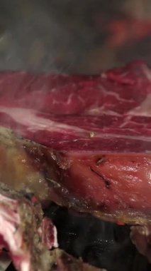 Restoran mutfağında kömür ızgarasında pişen enfes Floransa bifteği, yükselen duman.