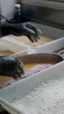 Profesyonel aşçı ince et dilimlerini un ile pişirir, yumurtalara batırır, ekmek kırıntılarıyla kaplar, bir restoran mutfağında kakao hazırlar.