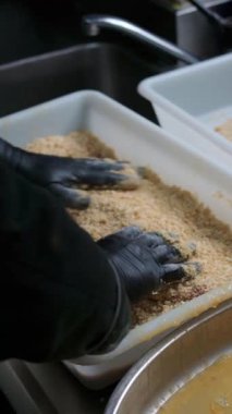 Profesyonel aşçı eldiven giyiyor, geleneksel kakao pirzolasını ticari restoran mutfağında ekmek kırıntılarıyla ekiyor, klasik asturyan mutfağı spesiyalitesi hazırlıyor.