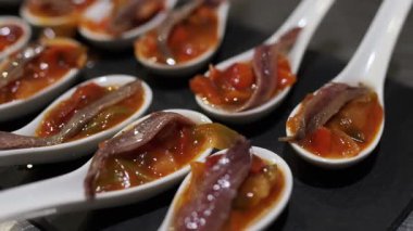 Çağdaş seramik kaşıklar ançüezle süslenmiş ratatouille, rafine mutfak sunumuyla koyu arka planda dinleniyor.