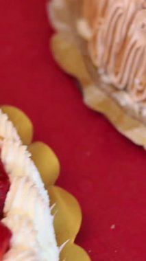 Çilek, çikolata ve karamel aromalı çeşitli dekore edilmiş keklerin kırmızı masa örtüsü üzerinde sergilendiği yakın plan çekimler.