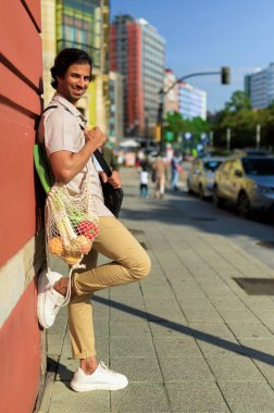 Hintli işadamı şehir kaldırımında tekrar kullanılabilir bir çantada erzak taşıyor, sürdürülebilirliği ve sağlıklı şehir yaşamını destekliyor.