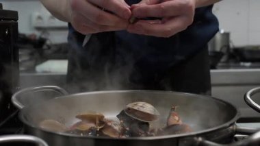 Profesyonel aşçı deniz ürünleri pilavı hazırlıyor. Restoranın mutfağına istiridye ekliyor.