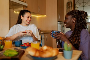 Mutlu lezbiyen çift taze meyve ve kruvasan yiyor, portakal suyu, kahve ya da çay içiyor, mutfaklarında birlikte kahvaltı yapıyorlar.