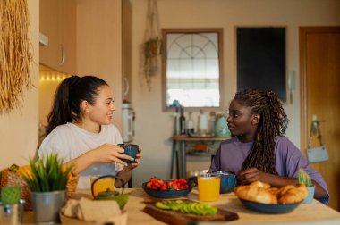 İki kadın, sıcacık mutfaklarında sağlıklı ve lezzetli bir kahvaltı yapıyorlar, birbirlerine eşlik ediyorlar.