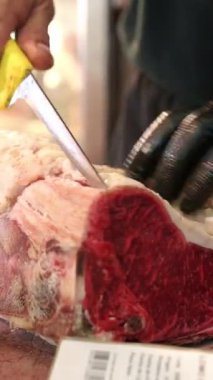 Kasap büyük bir pirzola dilimini ustalıkla budar ve hazırlar. Etin mermer ve kalitesini gösterir.