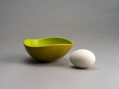 Still life of a green cup with a wooden egg, on a gray background clipart