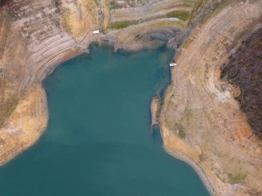 Sahil şeridi ve tekneleri açık olan sakin bir göl manzarası. Havadan çekilen bir görüntüde çıplak toprak ve kaya oluşumlarının yer aldığı sakin bir göl ve kıyı şeridi sergileniyor.. 