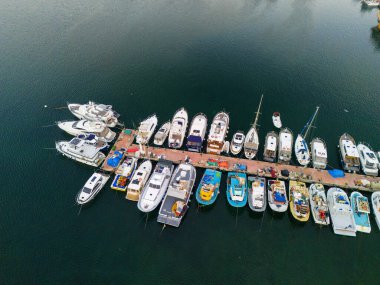 Aerial View of Colorful Boats Docked at a Marina. High-angle, full shot of various boats, from yachts to smaller vessels, neatly arranged at a marina.  clipart