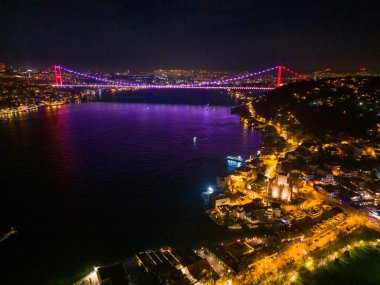 İstanbul 'un Gece Boğazı Köprüsü, canlı renklerle aydınlatılmış. İstanbul, Türkiye 'deki Boğaz Köprüsü' nün gece hava görüntüsü, canlı ışığını göstererek karanlık suları yansıtıyor..