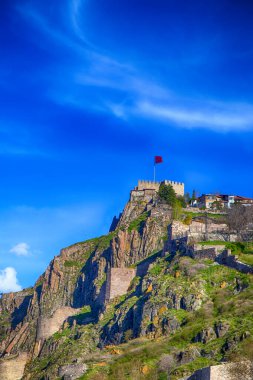 Ankara Şatosu, Ankara 'nın en yüksek yeri. Tepesinde Türk bayrağı, kalenin duvarları, mavi ve bulutlu bir gökyüzü. Turistlerin Ankara, Anadolu ve Türkiye 'yi ziyaret edeceği ünlü bir yer.
