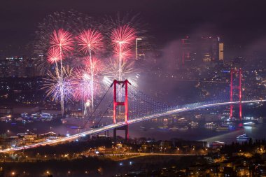 İstanbul 'un aydınlatılmış Boğaz Köprüsü ve şehir manzarası üzerinde havai fişeklerin uzun süre patlayacağı çarpıcı bir çekim, seyahat ve kutlama temaları için mükemmel.