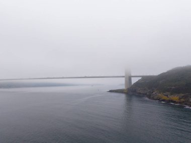 Suyun Üzerindeki Puslu Köprü, Huzurlu Sahil Sahnesi. Bir su kütlesini, fiyort ya da boğazı kaplayan ve hafif bir sisle örtülü bir köprüyü gösteren sakin bir manzara. Yavuz Sultan Selim Köprüsü Türkiye