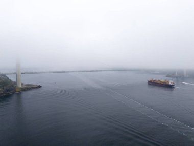 Kargo gemisi ve liman yapılarıyla puslu liman manzarası. Hafif bir sisle kaplanmış bir limanın havadan tam görüntüsü. Yavuz Sultan Selim Köprüsü İstanbul Türkiye Beykoz Poyrazkoy Anadolu 