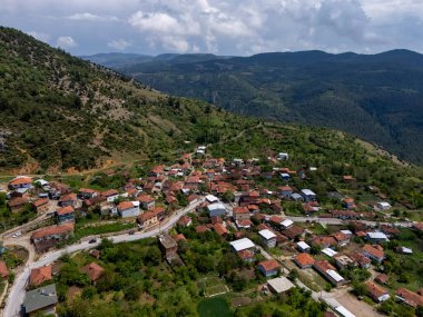 Türkiye 'nin Bursa kentindeki Gelemi köyünün yeşil dağlara kurulmuş havadan görünüşü. Geleneksel kırmızı çatılı evler ve dolambaçlı yollar parçalı bulutlu bir gökyüzünün altında huzurlu bir kırsal alan yaratır. Türkiye