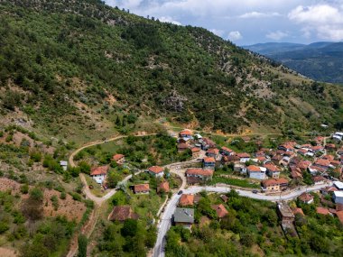 Bursa, Türkiye 'deki Gelemi köyünün havadan görüntüsü. Geleneksel evler tepenin yamacına dağılmış, kıvrımlı yollar ve yeşil manzarayla çevrili, bulutlu bir gökyüzünün altında orman dağlarıyla çevrili. 