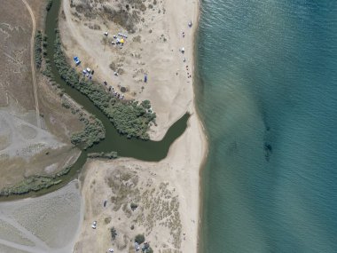 Türkiye 'nin Enez kenti yakınlarındaki kumlu bir sahilde denize dökülen bir nehrin yukarıdan aşağı havadan görüntüsü. Kampçılar, çadırlar ve doğal bitki örtüsü yaz güneşi altında huzurlu bir manzara yaratır..