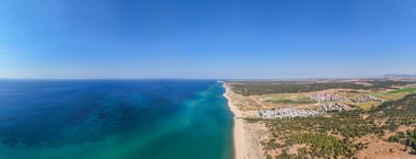 Saros Körfezi ve Türkiye 'nin Edirne kentindeki Enez kıyı kasabasının panoramik hava manzarası, turkuaz sular, kumlu plaj, yeşil orman ve mavi gökyüzü altında huzurlu bir yaz manzarasına sahip.