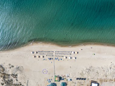 Turkuaz deniz boyunca şemsiyeleri ve güneşliği olan el değmemiş kumlu bir sahil manzarası. Türkiye 'nin Saros Körfezi' nde dinlenmek, güneşlenmek ve deniz kenarında keyif yapmak için ideal bir tatil beldesi.