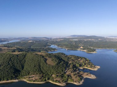 Berrak bir gökyüzü altında yoğun yeşil ormanlar ve sakin mavi suyla çevrili Merli Barajı 'nın havadan görünüşü doğal güzellik ve sükuneti, seyahat, doğa ve çevre temaları için idealleri vurguluyor..