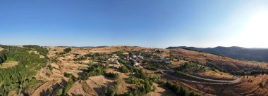 Boyabat, Sinop 'taki Kurtlu Köyü' nün panoramik hava manzarası. Geleneksel kır evleri, dolambaçlı yollar ve açık mavi gökyüzünün altındaki tepeler huzurlu bir doğal ortamda yer alıyor..