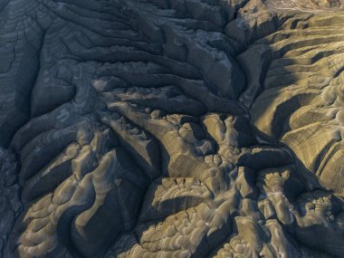 Aşınmış tepelerin dramatik gölgeleri ve katmanlı dokularıyla drone görüntüsü. Doğal arazi şekilleri soyut, sanatsal bir manzara yaratır. Arkaplan, baskı ve yaratıcı tasarım için mükemmeldir..
