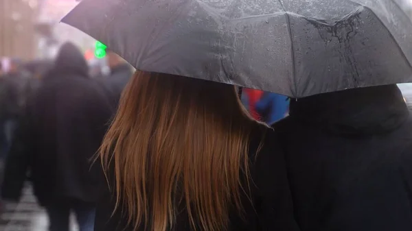 Couple under an umbrella walking down the street where. Young people walking under the umbrella under the rain